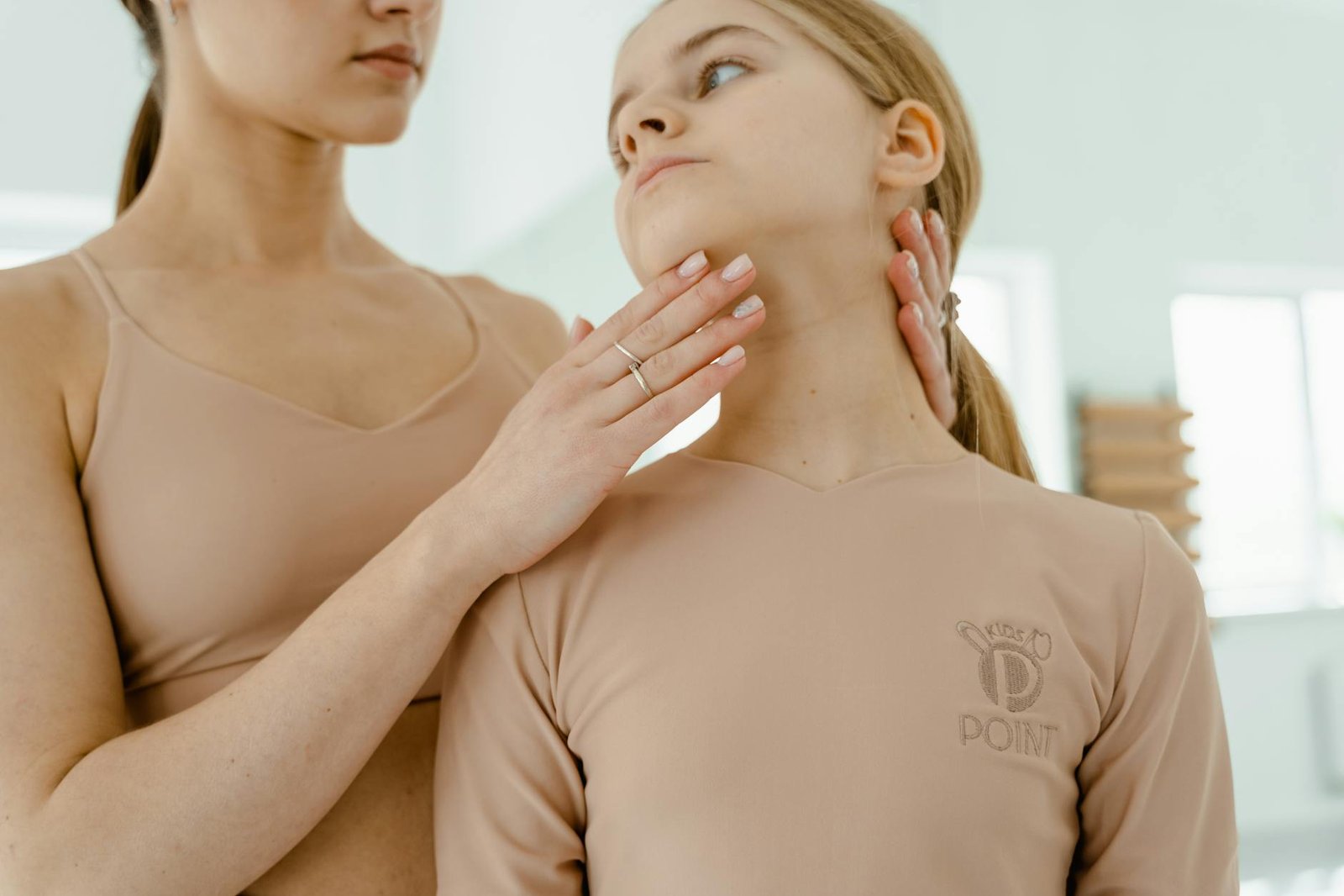 A ballet teacher gently adjusts a young dancer's posture during a class, emphasizing grace and elegance.
