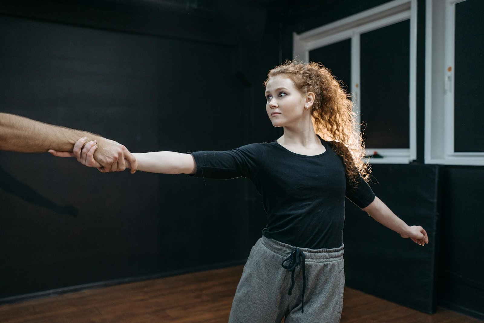 A young woman dancer holds hands with a partner during a ballet practice.