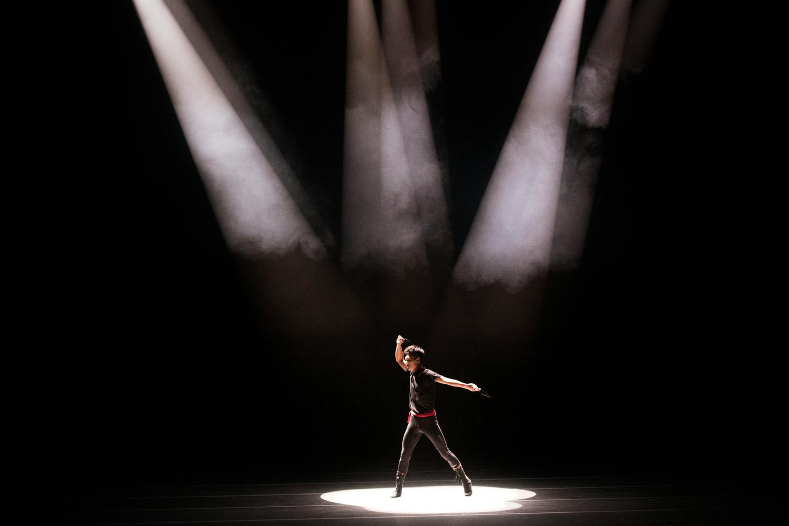 Energetic performance by male dancer under dramatic stage lighting.