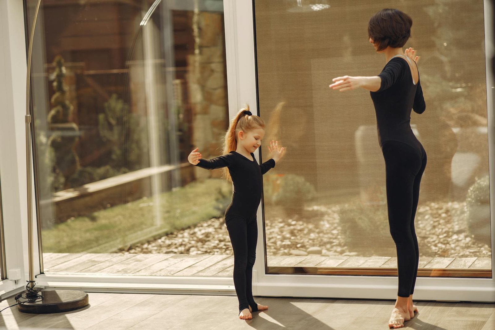 A mother and daughter practice ballet in matching leotards indoors, showcasing bonding and grace.