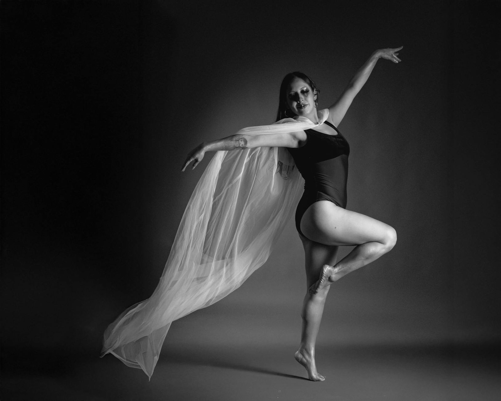 A graceful ballerina poses in a black and white studio setting, exuding elegance and strength.