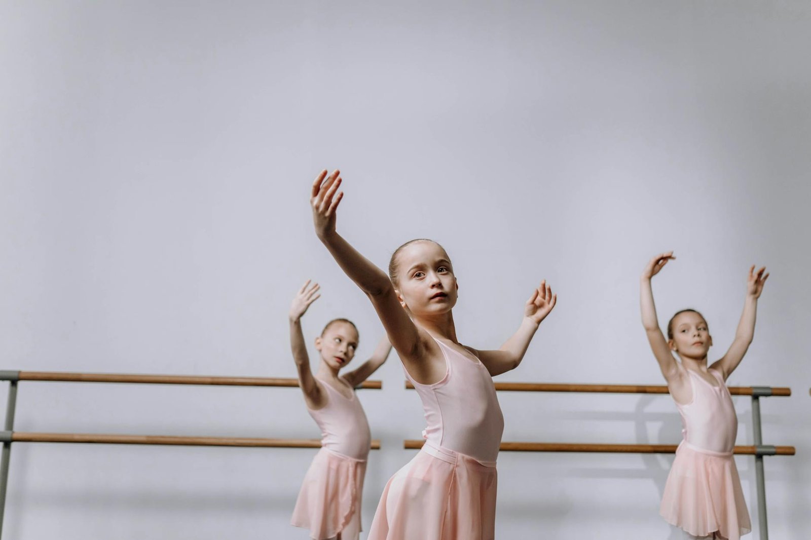 Three young ballerinas in pink tutus practice in a ballet studio, showcasing graceful choreography.