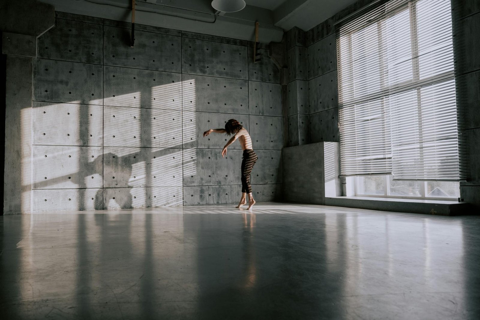 A solitary dancer practices gracefully in a sunlit modern dance studio.