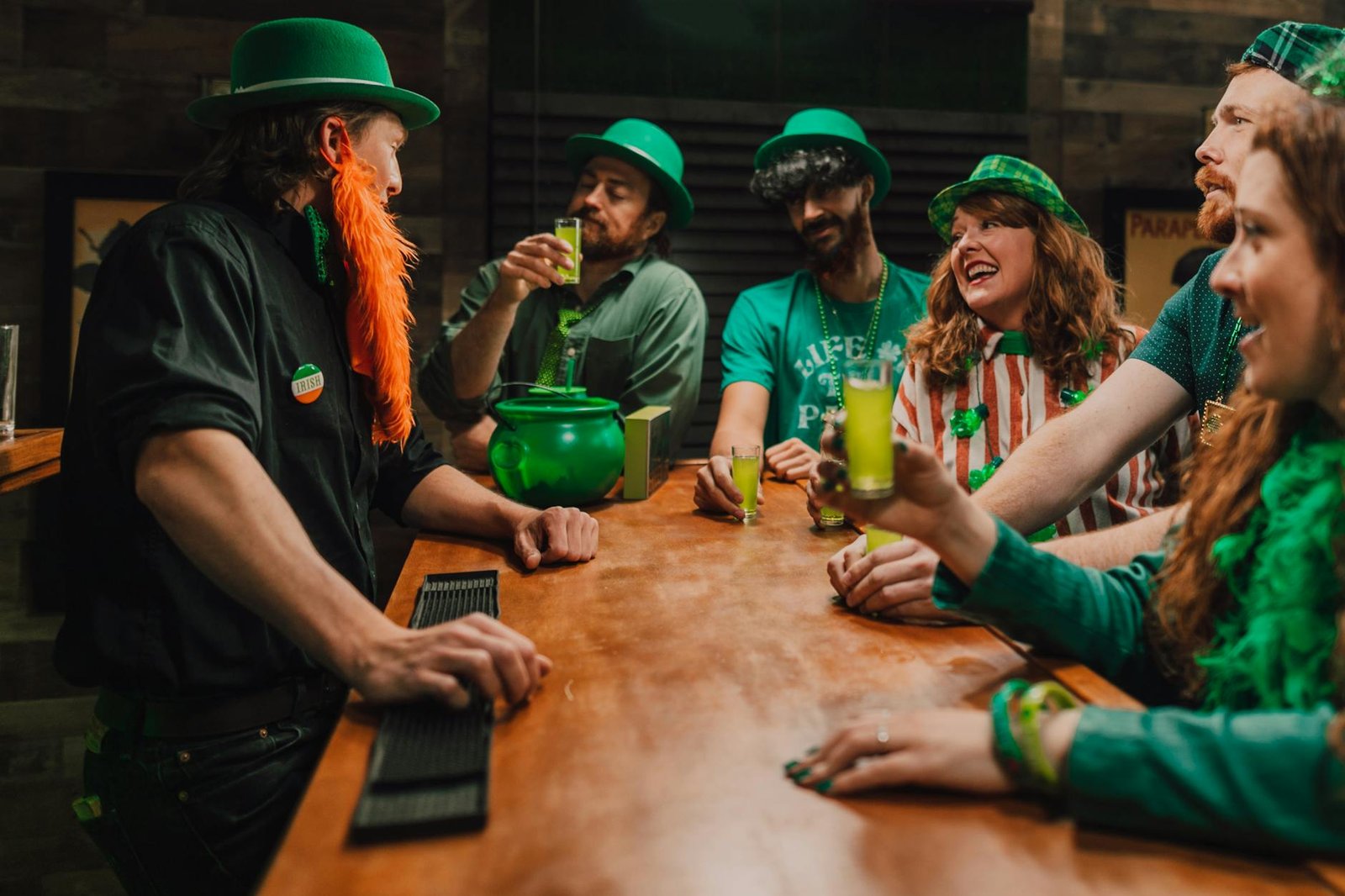 Group of friends enjoying drinks and laughter at a St. Patrick's Day party in a bar setting.