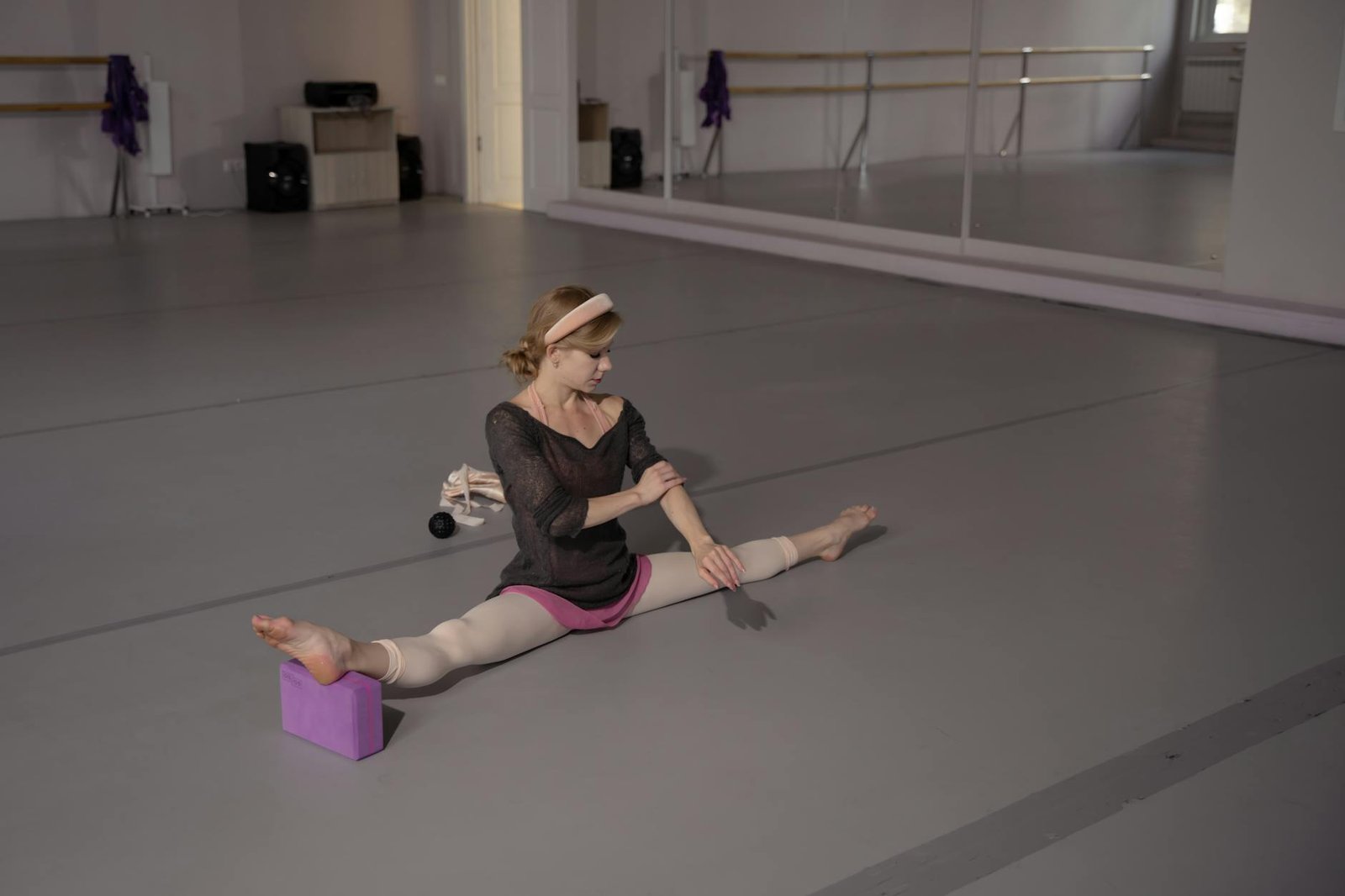 A ballet dancer performs a leg split while stretching on the floor of a dance studio.