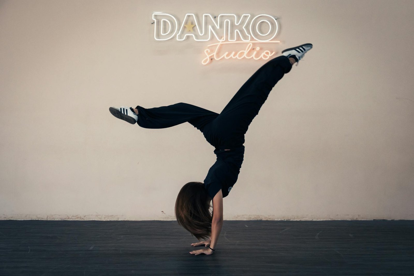Athletic young woman doing a handstand in Danko studio under neon lights.