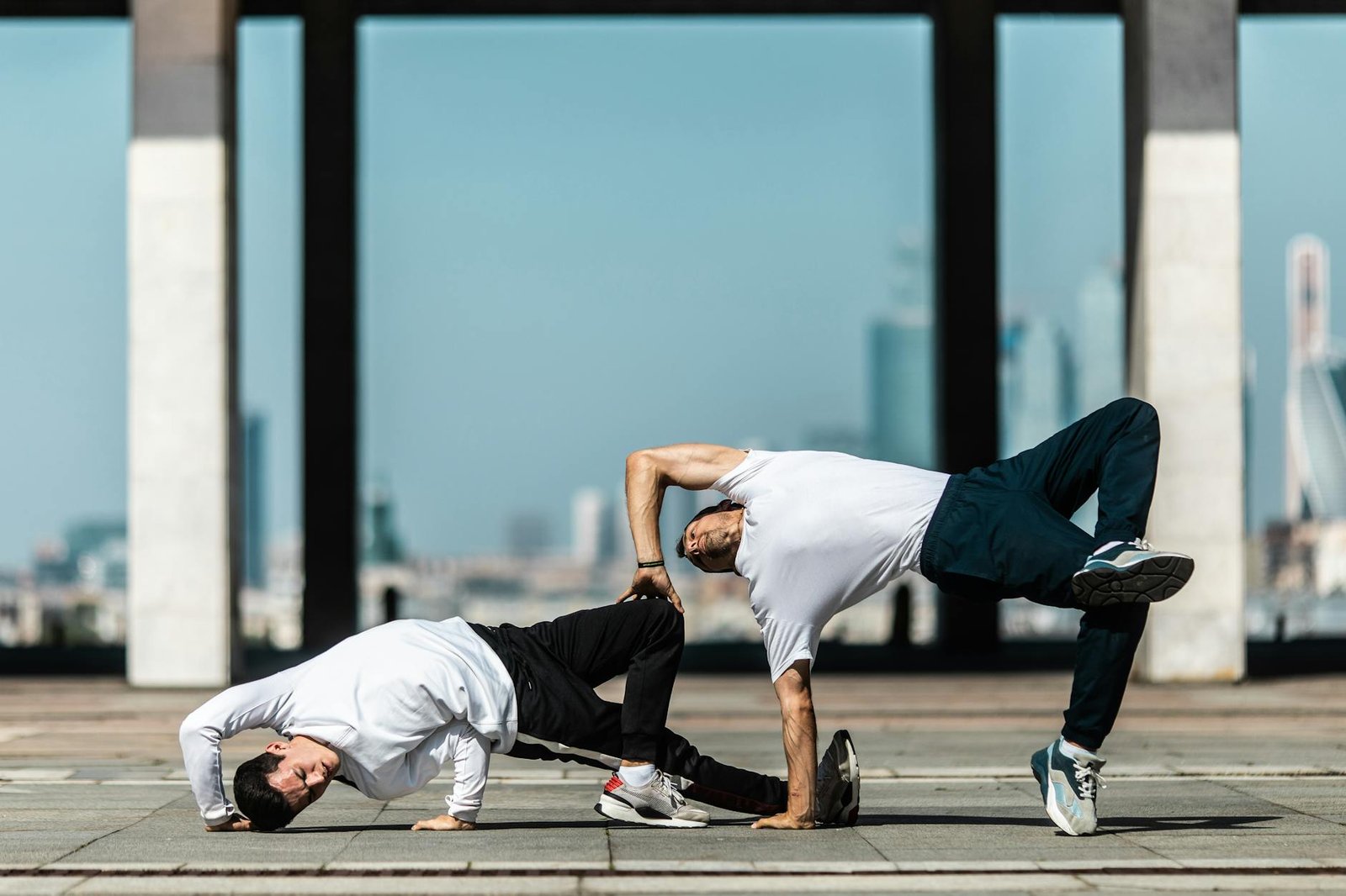 Two men performing breakdance moves on a city street under a clear sky.