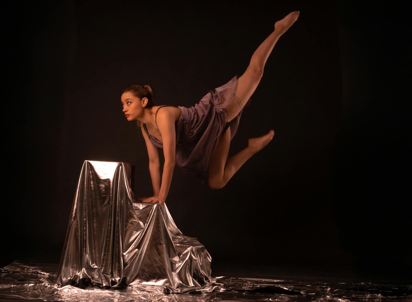 A talented female dancer performing an elegant leap on a dark studio stage.