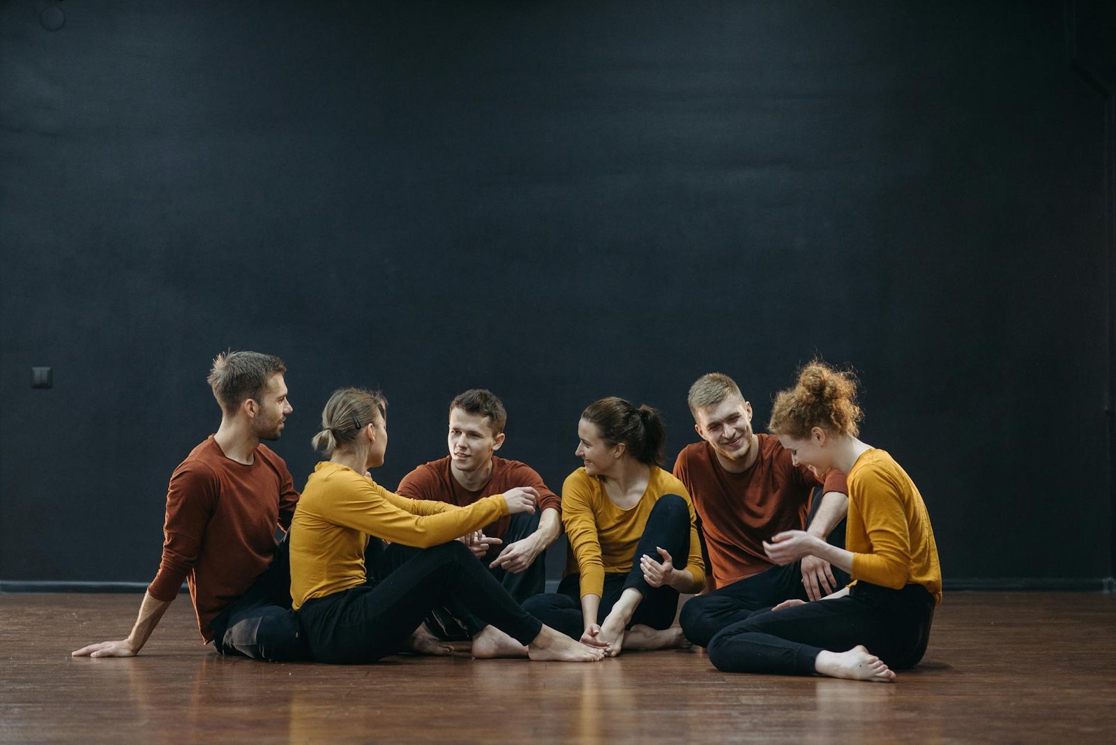 Casual group of adults relaxing in a dance studio with wooden floors and dark walls.