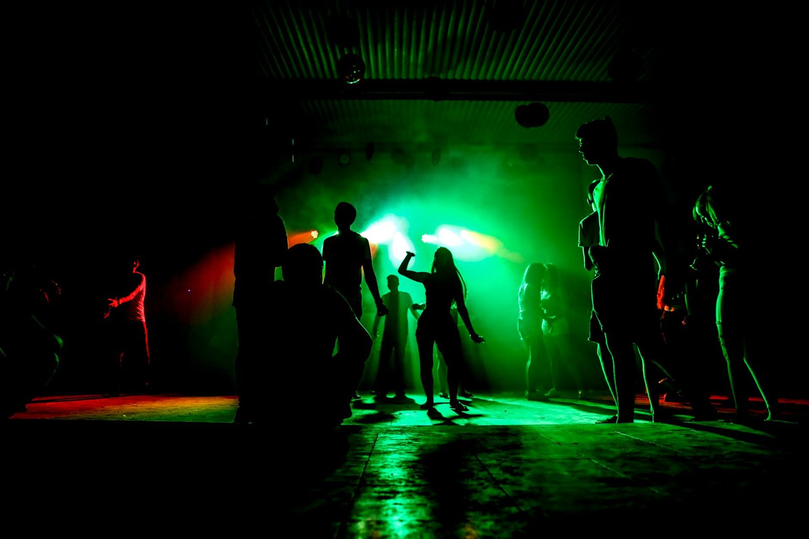People dancing in a nightclub with colorful green lighting and vibrant atmosphere.