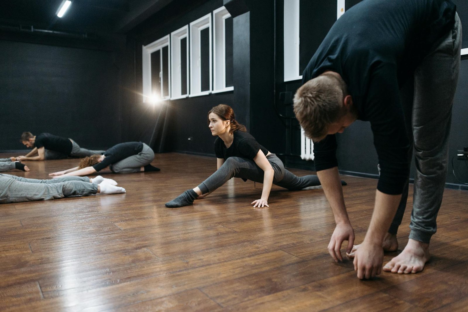 A group of adults stretching on wooden flooring in a fitness studio.