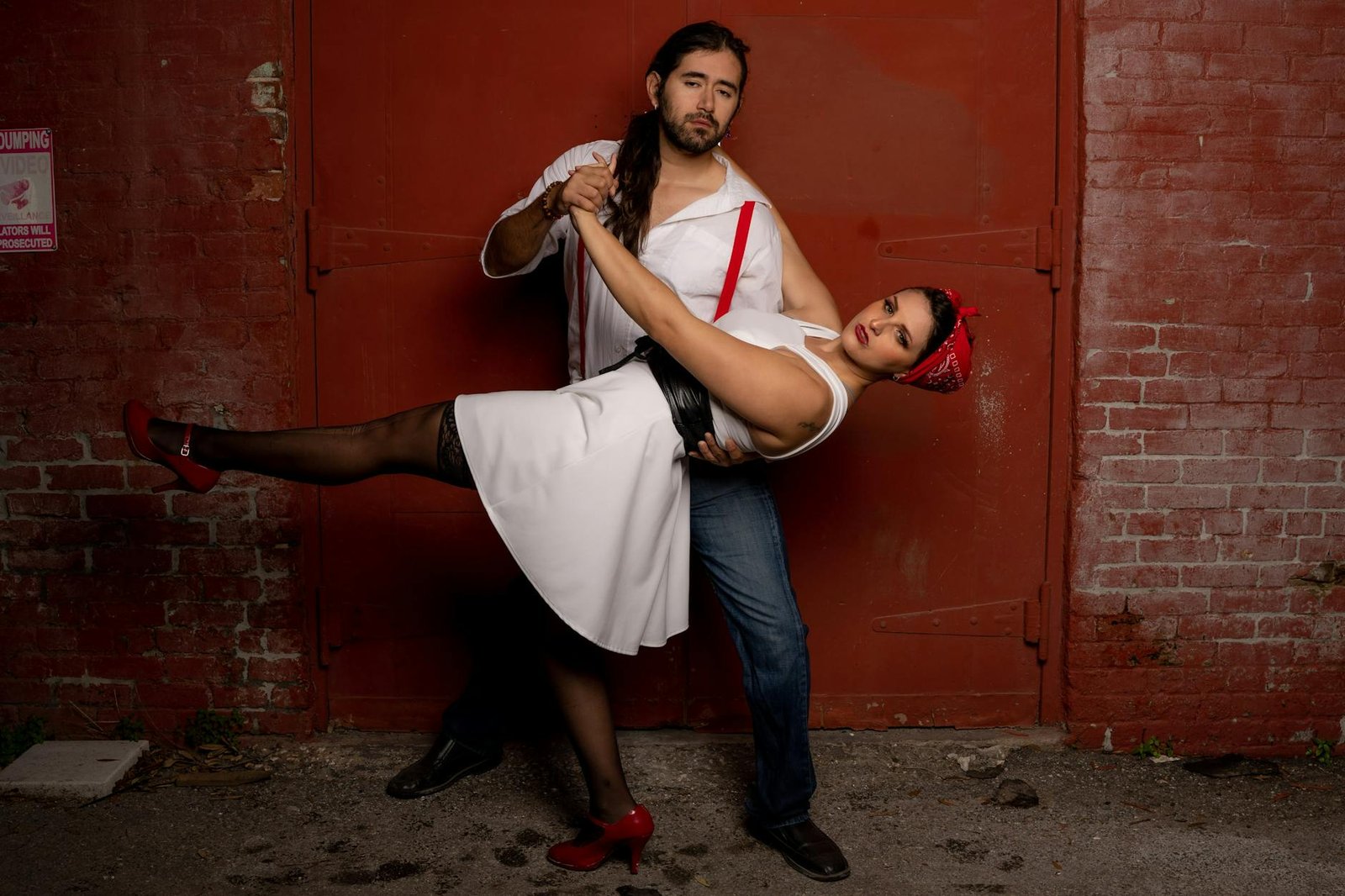 A couple dances gracefully in urban setting, against a rustic red brick wall, exuding energy and charm.
