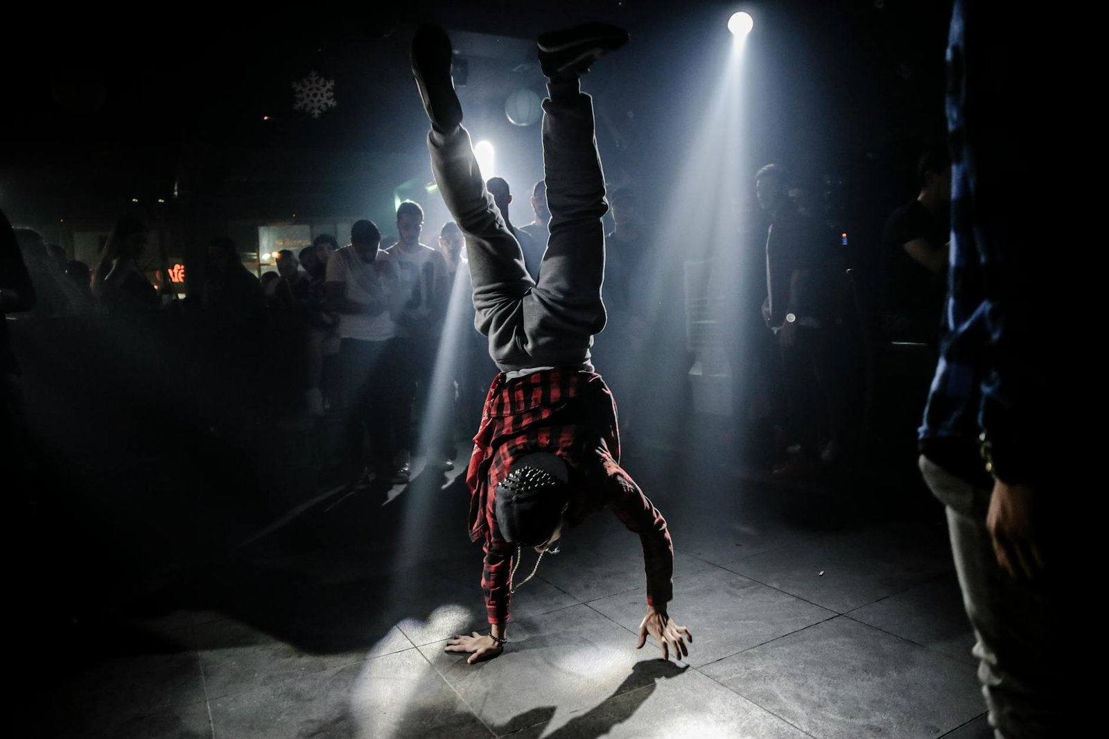 Breakdancer in plaid shirt performs a handstand in a lively club setting.