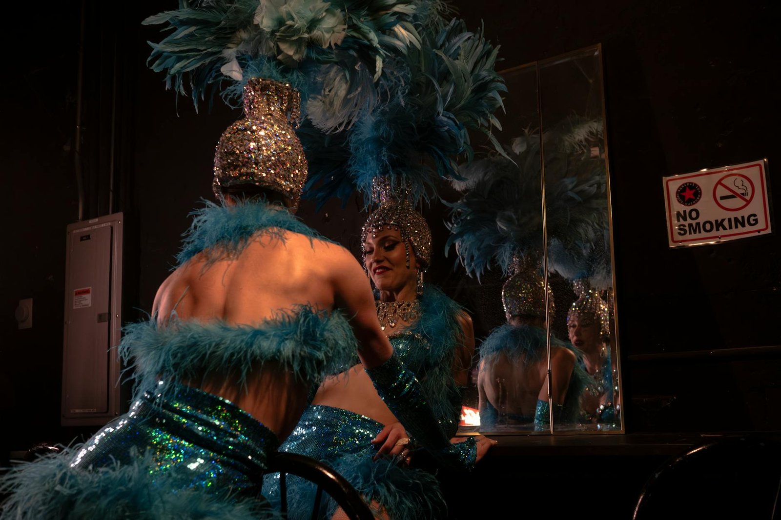 Showgirl in vibrant costume backstage, preparing for a dazzling performance with feathers and sequins.
